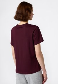 Bordeauxkleurig T-shirt met korte mouwen en een ronde hals, gemaakt van zachte katoen. De achterkant heeft een eenvoudige, strakke uitstraling zonder afbeeldingen of versieringen.