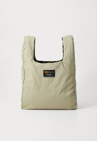 Khaki torba na ramię z kwadratowym otworem; wykonana z miękkiego, teksturowanego materiału; posiada czarną naszywkę z logo z przodu oraz wzorzyste wnętrze.