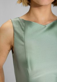 Abito verde in satin con busto aderente e scollatura a V, caratterizzato da una texture liscia e linee pulite. Senza chiusure visibili o motivi.