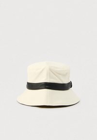 Κρεμ χρώματος καπέλο τύπου bucket με μαύρη υφασμένη ταινία, διαθέτει φαρδύ γείσο και στρογγυλή κορυφή, κατασκευασμένο από ανθεκτικό ύφασμα.