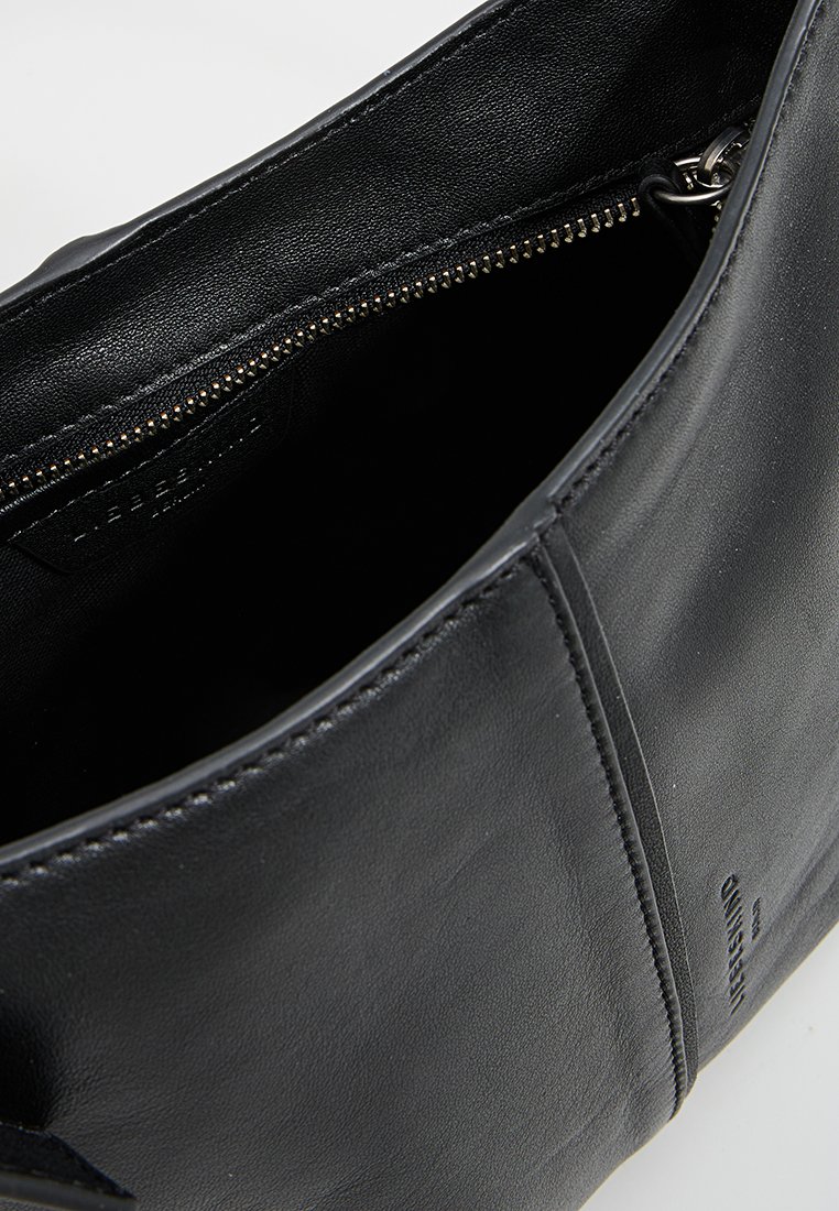 Schwarze Lederhandtasche mit Reißverschluss, glatter Textur und minimalistischen Design. Das Innere hat eine weiche Fütterung und keine Fächer.