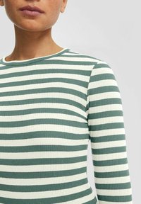 Top à manches longues en tissu côtelé, présentant des rayures alternées en vert et crème. L'encolure est ronde, avec des manches ajustées.