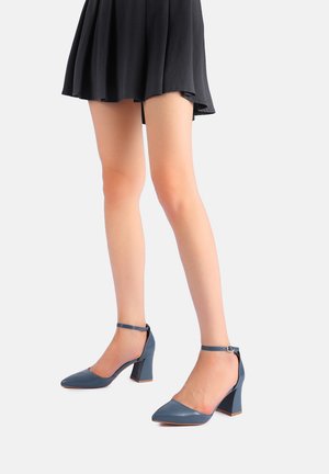 Scarpe con tacco alto in pelle lucida blu, con punta affilata e cinturino alla caviglia, dotate di un tacco a blocco per maggiore stabilità. Superficie liscia e lucida.
