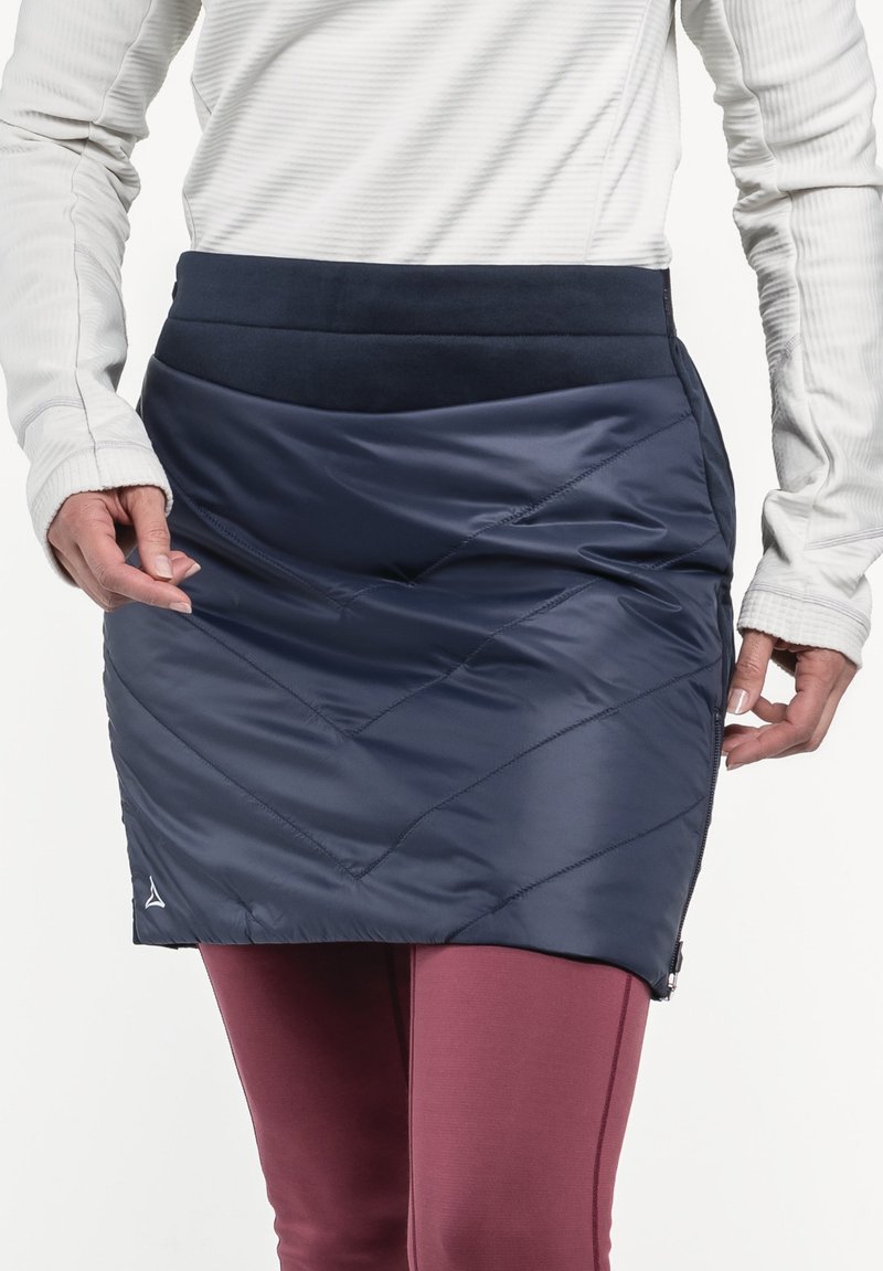 Marineblauer isolierter Rock mit diamantgepatchtem Design und elastischem Bund, kombiniert mit bordeauxroten Leggings. Reißverschlussdetails an der Seite.