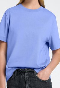 Jasnoniebieska bawełniana koszulka z krótkim rękawem i okrągłym dekoltem, o luźnym kroju i gładkiej teksturze. W komplecie z wysokim stanem czarnymi dżinsami.