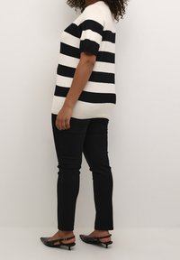 Gestreept gebreid top in zwart en wit met korte mouwen, gecombineerd met zwarte slim-fit jeans en zwarte slingbackschoenen. Soepele textuur.