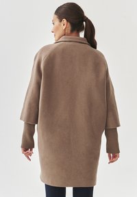 Bruine oversized jas met een hoge kraag, brede mouwen en een structuurstof, met ribbelmanchetten en een gladde afwerking op het lichaam.