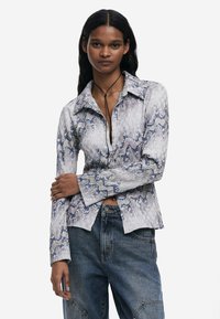 Košeľa s dlhým rukávom so zapínaním v textúrovanom, vlnitom modro-bielom vzore. Má golier a rozšírené manžety. V kombinácii s džínsami.