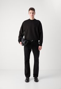 Sweatshirt nero con girocollo, abbinato a jeans neri e scarpe nere. Tiene una borsa in pelle nera. Colore solido e design minimal.