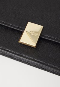 Black leather handbag with a textured surface and a gold triangular metal clasp featuring the brand name embossed on it.