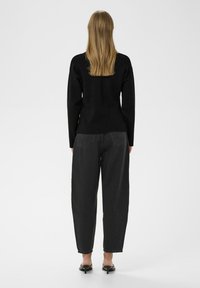 Melnā garām piedurknēm augšdaļa ar pieguļošiem pleciem; apģērbts ar augstām tumši pelēkām platām biksēm; plāni augstpapēžu melni apavi.