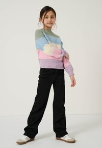 Sweater de malha com riscas horizontais em verde, azul, rosa e lavanda, combinado com jeans largos pretos e ténis brancos.
