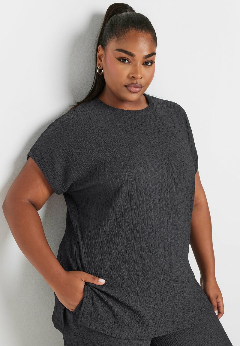 Tummanharmaa lyhythihainen paita, jossa on tekstuuroitu, timanttikuvioinen kangas. Varustettu pyöreällä kaula-aukolla ja sivutaskuilla lisätoiminnallisuutta varten.