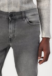 Jeans de mezclilla gris con un ajuste slim, que presentan una cintura recta, bolsillos frontales y detalles de desvanecimiento sutiles. La tela tiene una textura suave.