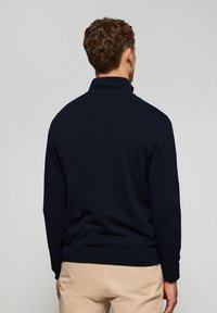 Suéter de color azul marino con un alto cuello, puños y dobladillo acanalados, hecho de un material de punto suave, que presenta un diseño limpio y sencillo.