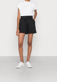 Shorts noirs avec une taille élastique et un cordon de serrage, dotés de poches latérales. Associés à un t-shirt blanc à manches courtes et des baskets blanches.