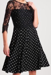 Svart klänning med spetsliv och trekvartslånga ärmar, med ett prickigt mönster. Urtjockad kjol och texturerad spetsdetalj.