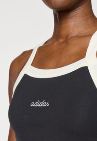 Juodas sportinis marškinėlis be rankovių su baltais kraštais, ant priekinės pusės išsiuvinėtu "adidas" logotipu. Medžiaga atrodo lygi ir prigludusi.