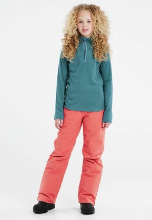 Fleece-Pullover in Türkis mit einem halbzerzipbaren Design, kombiniert mit korallenfarbenen wasserdichten Hosen. Schwarze Stiefel runden das Outfit ab. Weißer Hintergrund.