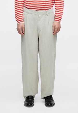 Pantaloni di lino grigio chiaro con vestibilità comoda, caratterizzati da una parte anteriore piatta e tasche laterali. Abbinati a scarpe nere e una maglia a righe rosse e bianche.