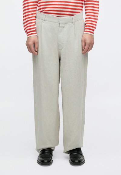Pantalon en lin gris clair à coupe décontractée, avec un devant plat et des poches latérales. Associé à des chaussures noires et un haut rayé rouge et blanc.