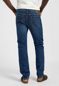 Jeans de mezclilla azul oscuro con un diseño de pierna recta, costuras visibles y una etiqueta de cuero marrón en la parte trasera de la cintura.