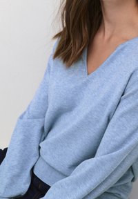 Light blue pullover sweater featuring a V-neck, long sleeves, and ribbed hem. Made from soft fabric with a smooth texture.