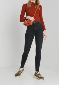 Jeans negros ajustados con cintura alta, combinados con una blusa roja de canalé y un pequeño bolso naranja. El calzado incluye zapatillas deportivas multicolores.