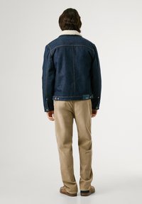 Chaqueta de denim con un collar de borrego sintético blanco, de color azul oscuro, con costuras en contraste, diseño ajustado, combinada con pantalones de color beige claro.