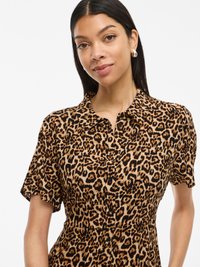 Rochie cu imprimeu de leopard, cu mâneci scurte, guler și design cu butoni în față. Material moale, bază de culoare bej deschis cu pete negre și maro închis.