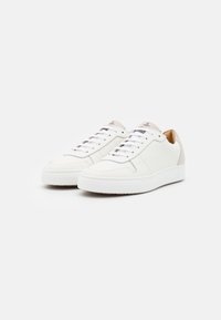 Bílé kožené tenisky s hladkým povrchem, s kontrastní taupe patní částí a světlým šedým doplňkem na bocích a tkaničkách.