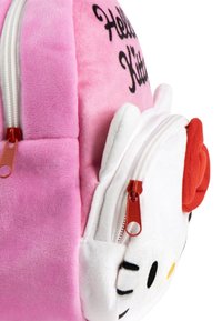 Sac à dos Hello Kitty en peluche rose avec une poche avant blanche, des tirettes de fermeture éclair rouges et un nœud rouge sur la tête de Hello Kitty.