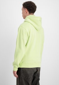 Felpa verde chiaro con un ampio cappuccio, polsini e vita a costine, abbinata a pantaloni grigi scuri. Il tessuto appare morbido e liscio.