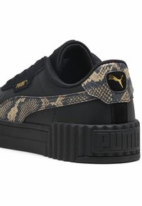 Baskets en cuir noir avec un accent en imprimé serpent texturé. Elles présentent une semelle rainurée et des coutures noires, soulignées par un logo doré sur le talon.