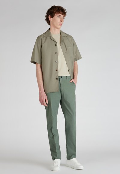 Olijfgroene short-sleeve shirt met knoopsluiting, gecombineerd met lichtgroene broek met een gestructureerd patroon en witte sneakers.