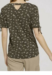 Top verde oliva con estampado floral, mangas cortas abullonadas, detalles atados y un escote en forma de llave en la parte posterior. Textura de tela suave, corte casual.