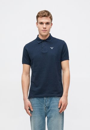 Ναυτικό πόλο μπλουζάκι από βαμβάκι, με γιακά, κοντά μανίκια και μικρό λογότυπο στο αριστερό μέρος. Συνδυάζεται με ανοιχτό μπλε τζιν.