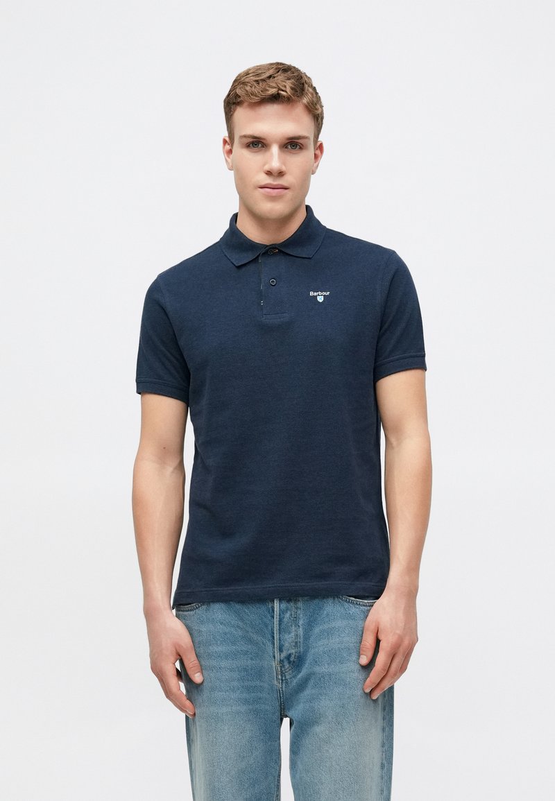 Ναυτικό πόλο μπλουζάκι από βαμβάκι, με γιακά, κοντά μανίκια και μικρό λογότυπο στο αριστερό μέρος. Συνδυάζεται με ανοιχτό μπλε τζιν.