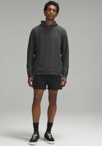 Hanorac gri texturat cu glugă, asortat cu pantaloni scurți negri și șosete negre, purtat cu adidași negri. Design simplu, casual și o croială lejeră.