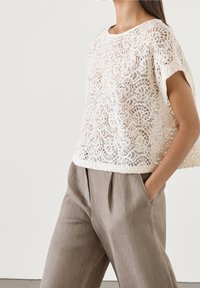 Haut blanc en maille dentelle avec encolure ronde et manches courtes, assorti à un pantalon en lin beige avec plis et poches latérales.