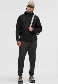 Svart zip-up jacka med huva, grå byxor, beige mössa och gula solglasögon. Texturerad tyg och figursydd design; har fickor och dragkedjor.
