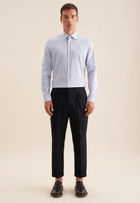 Camicia a righe blu con colletto slim, abbinata a pantaloni neri su misura e scarpe nere. Presenta righe verticali bianche e bottoni.