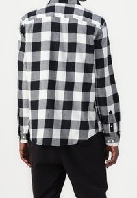 Camicia a maniche lunghe con bottoni in un motivo a scacchi bianco e nero, in tessuto di cotone, con orlo curvo e polsini con bottone.