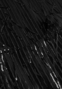 Schwarzer Stoff mit vertikalen Streifen und verstreuten Pailletten, der ein strukturiertes Muster aufweist, das Licht reflektiert und einen schimmernden Effekt erzeugt.