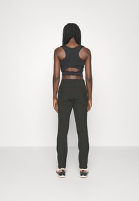 Top corto negro con un corte, combinado con pantalones ajustados verde oliva y zapatillas negras con detalles en blanco y naranja.