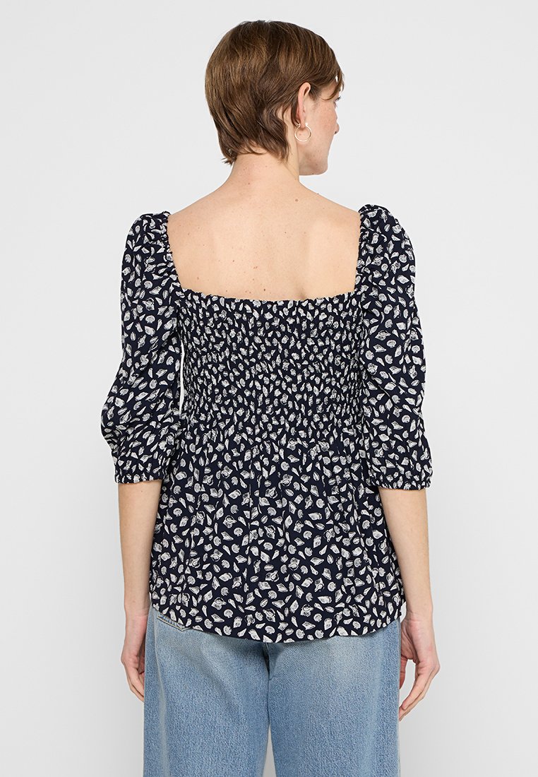 Marinebluse mit Puffärmeln, gerafftem Oberteil und weißem Blättermuster. Die Rückansicht zeigt einen quadratischen Ausschnitt und eine lockere Passform.