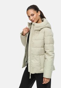 Giacca puffer beige chiaro con collo alto, chiusura con zip e tasche laterali. Presenta un design imbottito e una patch con il logo sulla manica.