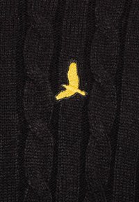 Schwarzer Strickstoff mit einem kleinen gelben Vogel, der in der Mitte im Flug gestickt ist.