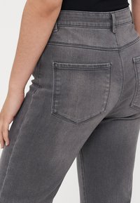 Jean en denim gris foncé taille haute, avec un design ajusté, deux poches arrière et une texture lisse. Coutures visibles au niveau de la taille.