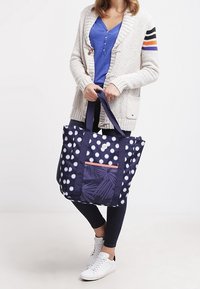 Borsa da tote blu navy con pois bianchi e tasca con cerniera rosa caratterizzata da un motivo a foglie. Manici solidi e materiale in canvas.